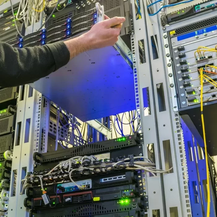 Technician inserting a server into a data center rack with various networking equipment and cables surrounding i