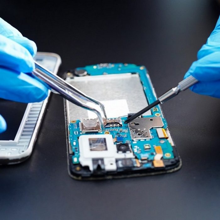 Technician with blue gloves repairs a smartphone’s internal circuit board using tweezers and a too